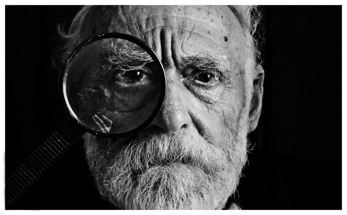 Old man with a magnifying glass over his eye