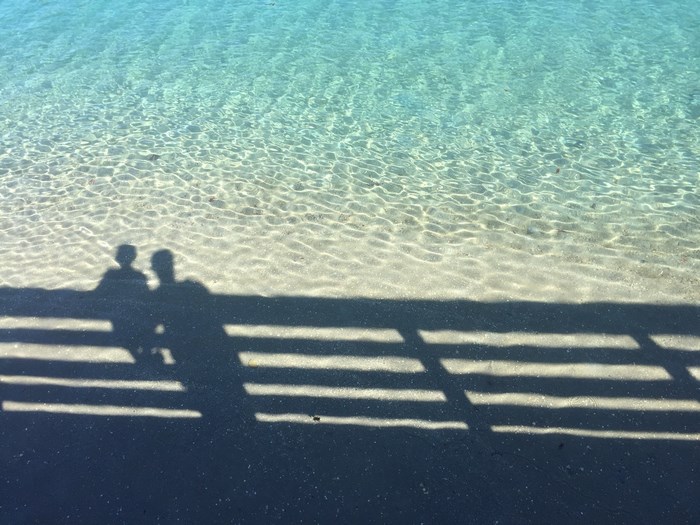 Shadows of two people on a beach with clear water