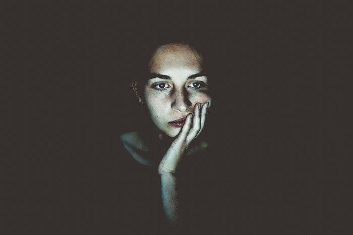 Woman with hand on face looking at screen in the dark