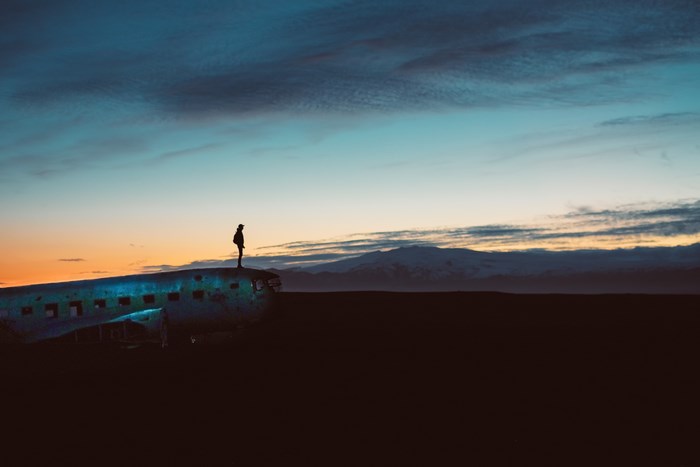 Person standing on abandoned airplane in Iceland at sunset
