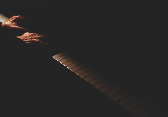 A hand plays a piano in dramatic lighting