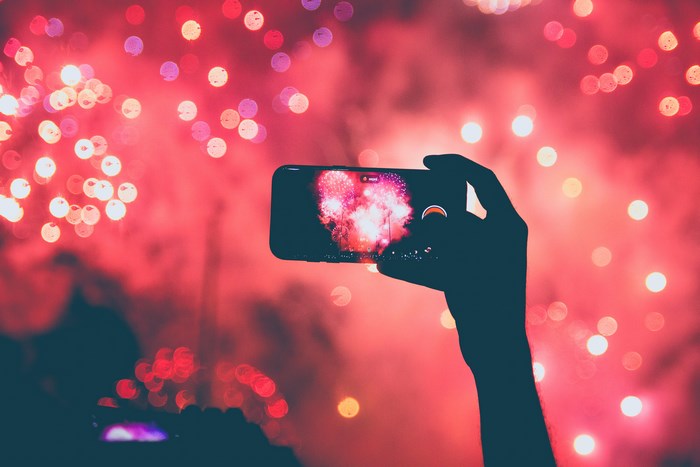 Hand holding iPhone recording fireworks at night