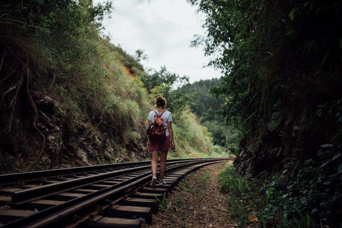 Woman with backpack walking on train tracks in nature