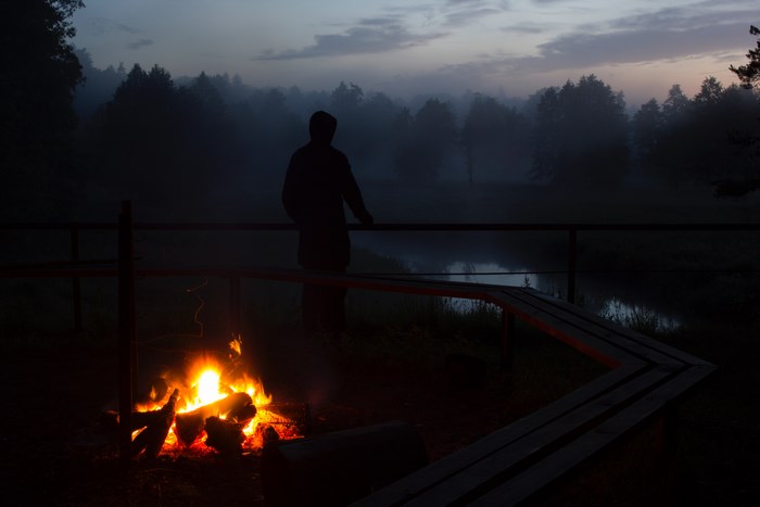 Silhouette by a campfire overlooking a misty forest and river