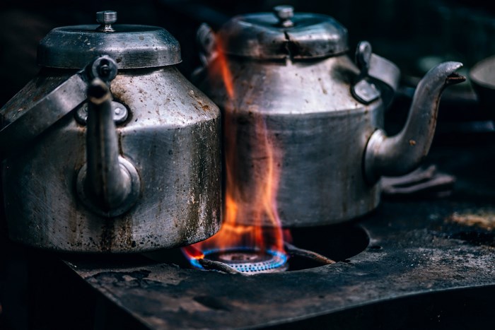 Two kettles heating on a gas stove with flames