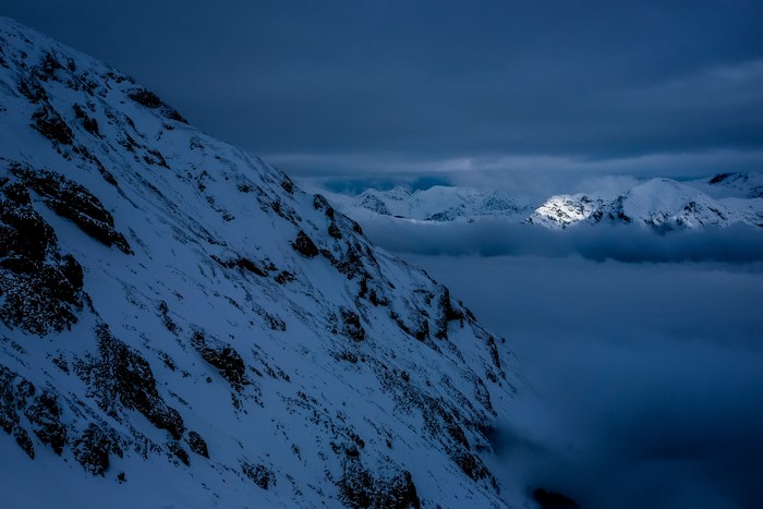 Snowy mountain peaks above clouds at dusk