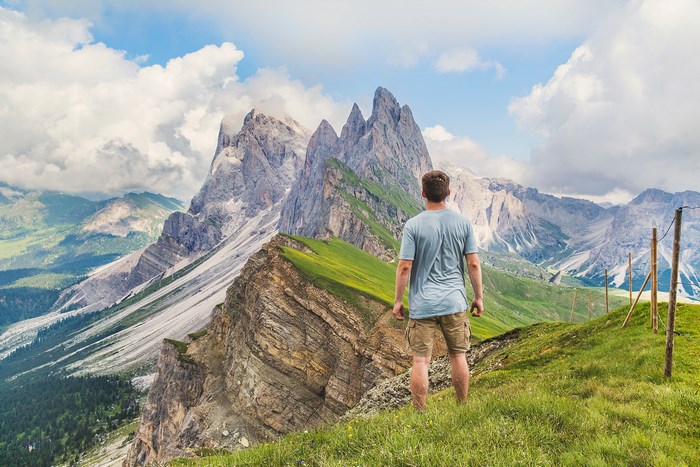Man standing on a grassy mountain ridge overlooking peaks