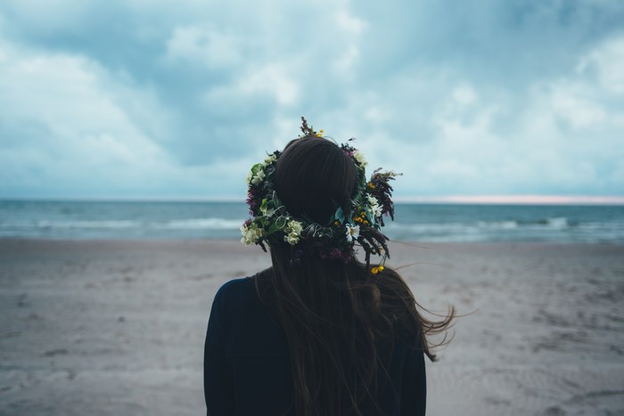 Woman with flower crown on beach looking at the sea