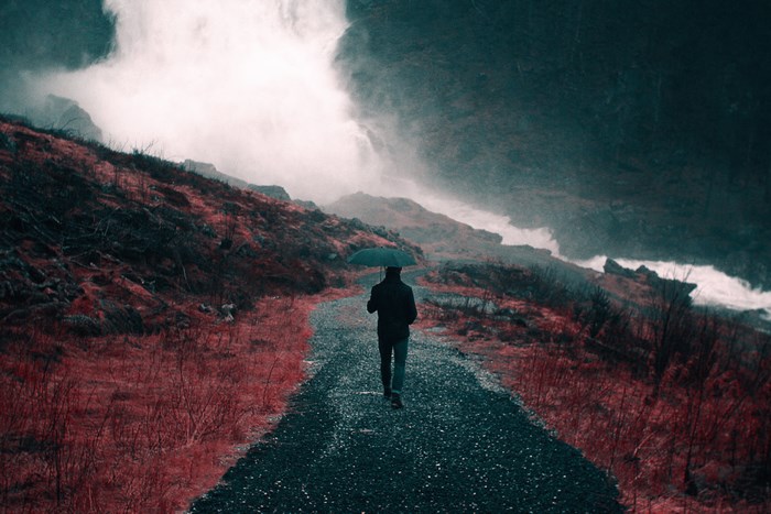 Man with umbrella walks on a path in a rocky landscape
