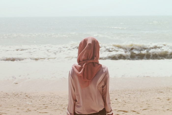Woman in pink hijab looking at the ocean waves