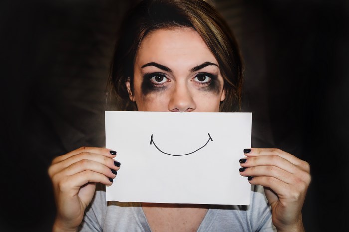 Woman with smudged makeup holding a drawing of a smile