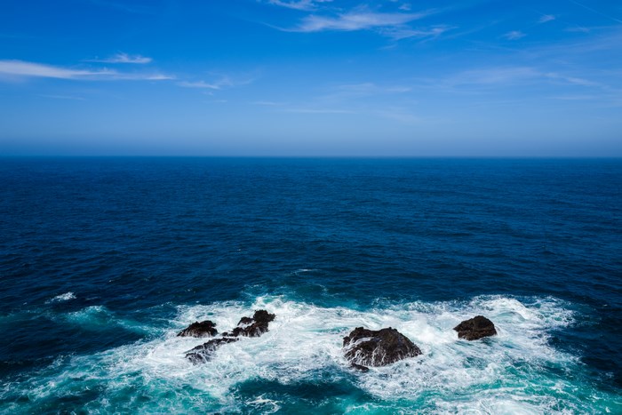 Ocean waves crashing against rocks under a blue sky