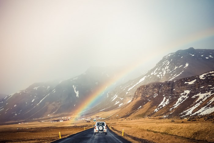 Car driving on road in Iceland with rainbow and mountains