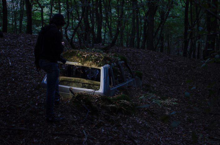 Man with flashlight inspects abandoned car in forest