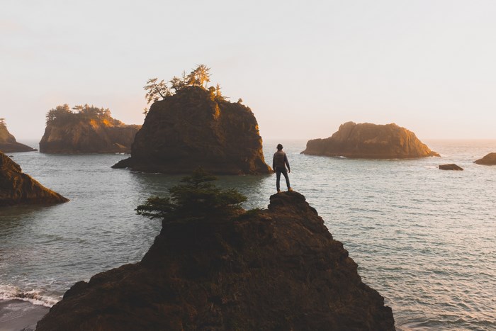 Man standing on a rock overlooking the ocean at sunset