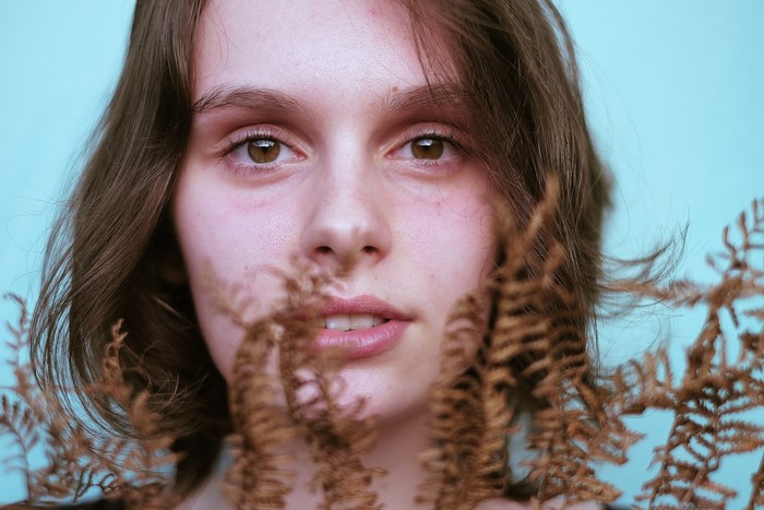 Woman with brown hair and brown eyes behind ferns