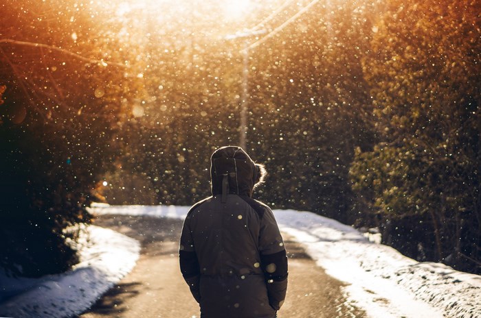 Person in fur-hooded jacket in snowy woods during golden hour