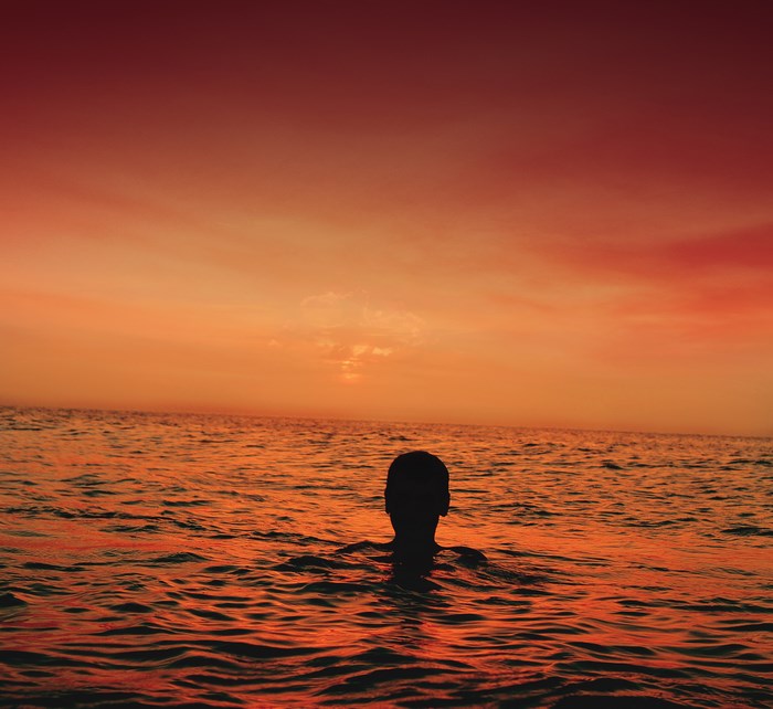 Silhouette of a person in the ocean at sunset