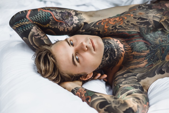 Man with full body tattoos lying on a white bed