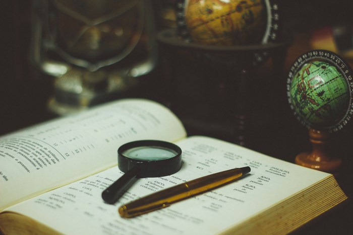 Open book with magnifying glass and pen on desk with globes