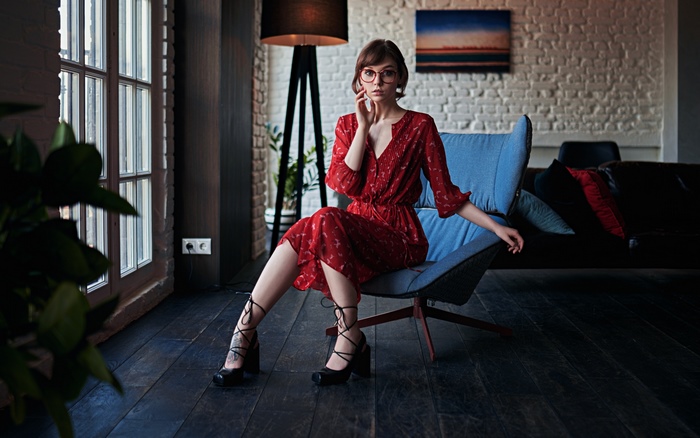 Woman in red dress wearing glasses sitting in a chair