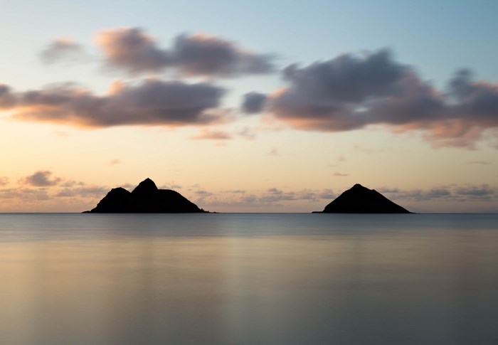 Two islands in the ocean at sunset with clouds