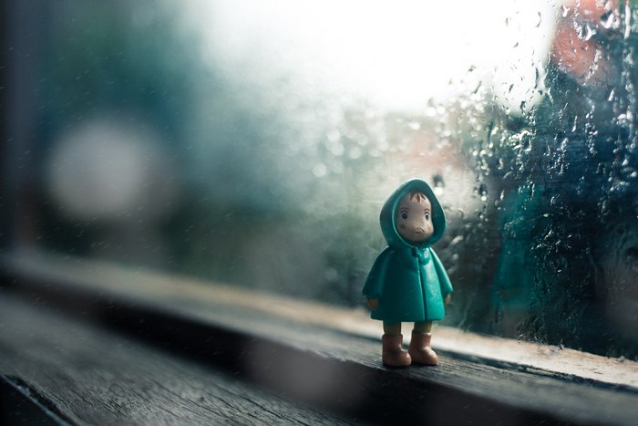 Toy in a raincoat by a rainy window