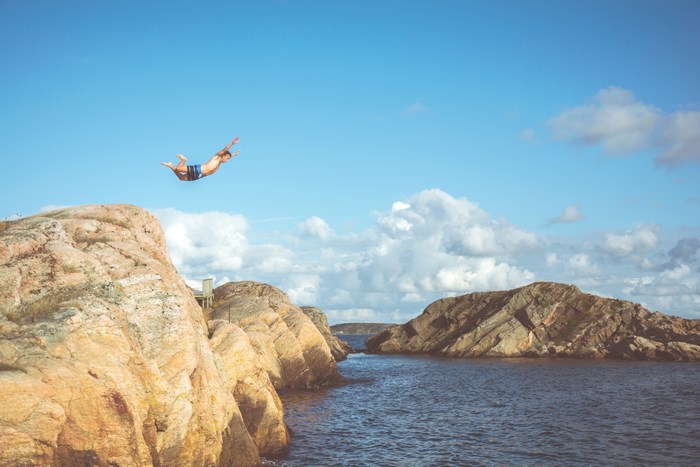 Man jumps off a rocky cliff into the ocean