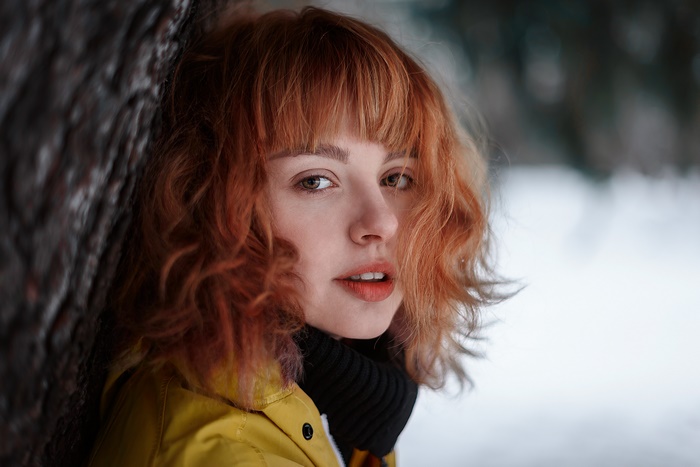 Woman with red hair leaning against a tree