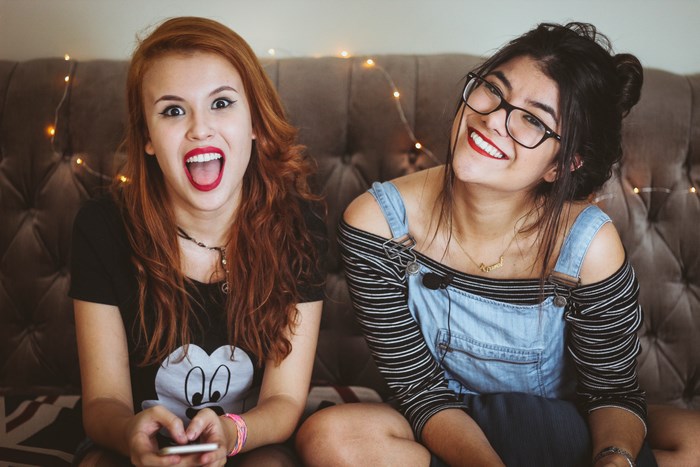 Two young women sitting on a couch with fairy lights