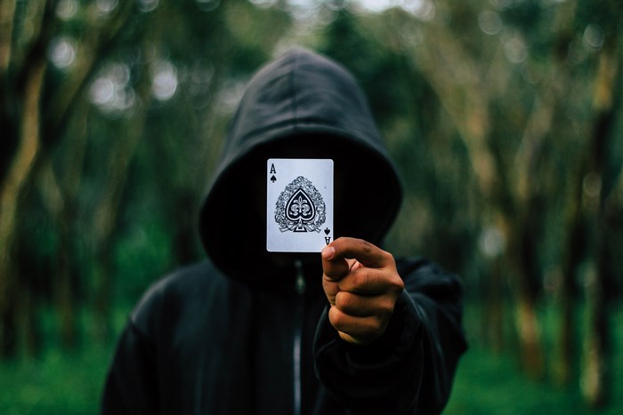 Person in a hoodie holding an Ace of Spades card