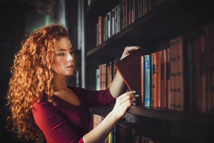Redhead woman selecting a book from a library shelf