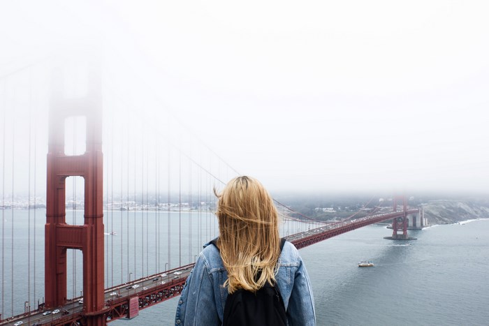 Woman with backpack looking at Golden Gate Bridge in fog