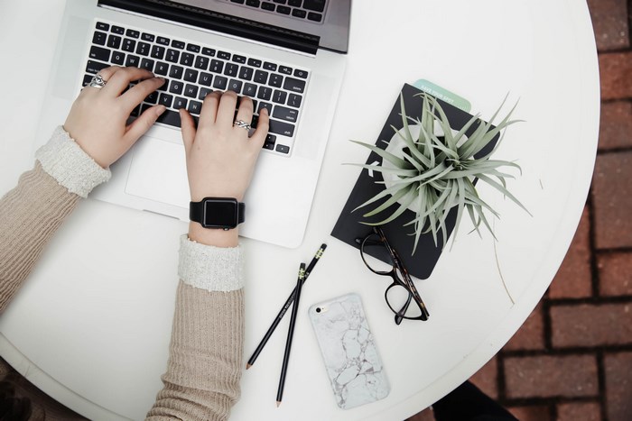Overhead view of hands typing on a MacBook with Apple Watch