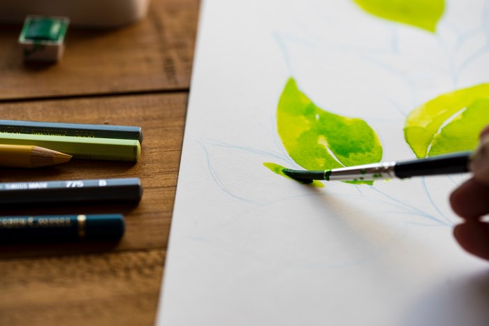 Watercolor painting of green leaves with pencils and brush