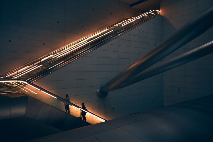 Two people on a brightly lit escalator in a dark subway station