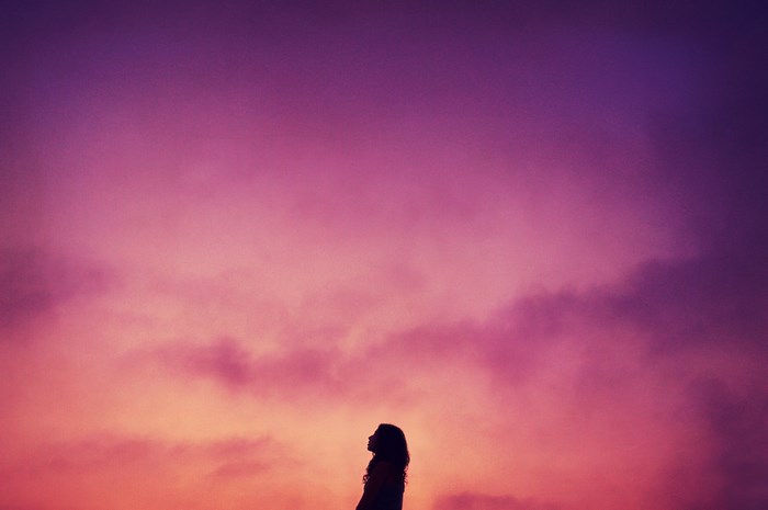 Silhouette of a girl looking up at a pink and purple sky