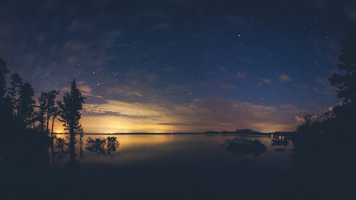 Night sky over a lake with boats and trees