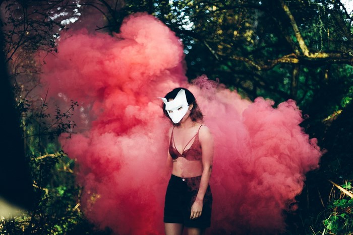 Woman in fox mask with red smoke bomb in forest
