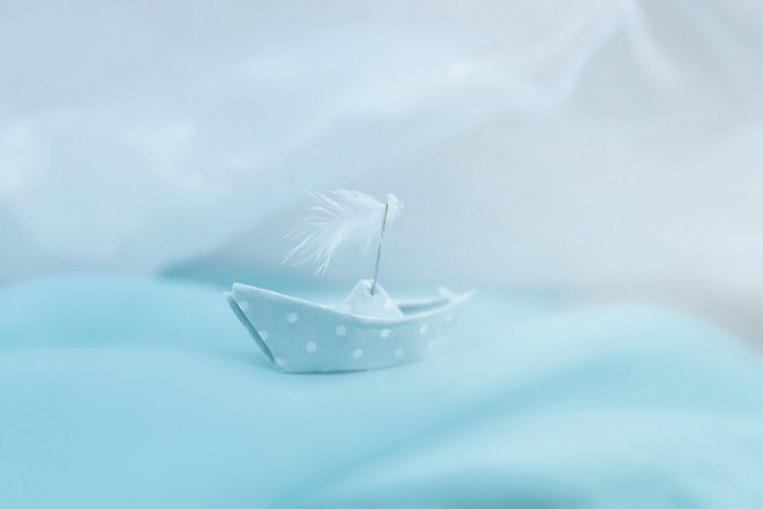 Origami paper boat with feather sail on blue fabric