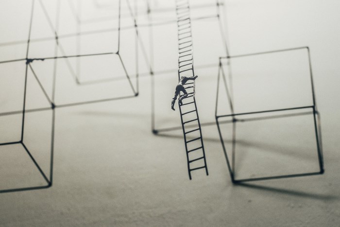 Miniature man climbing a ladder between abstract wireframes