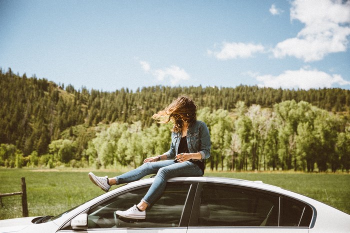 Woman sitting on car roof in a forest