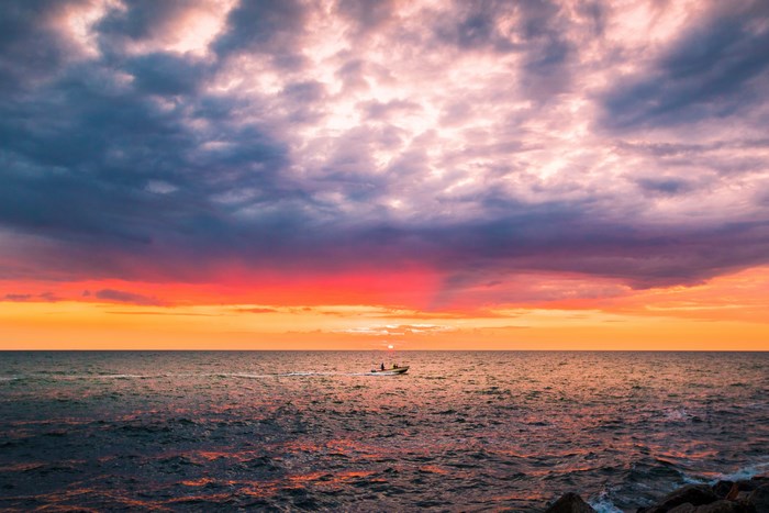 Motorboat on the ocean at sunset with colorful clouds