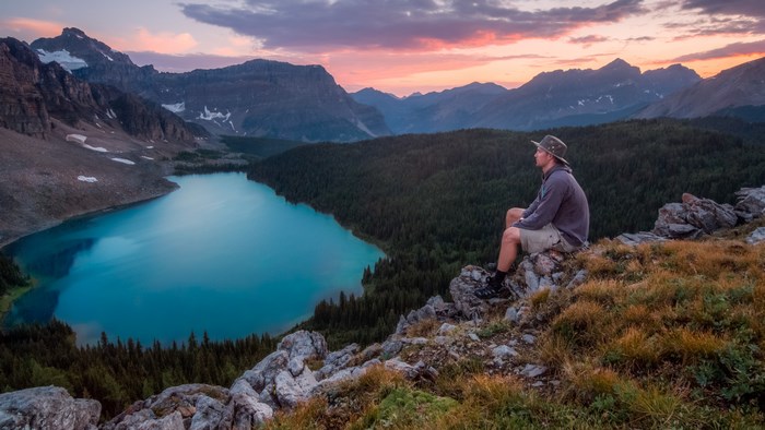 Man sitting on rocks overlooking a turquoise lake and mountains at sunset