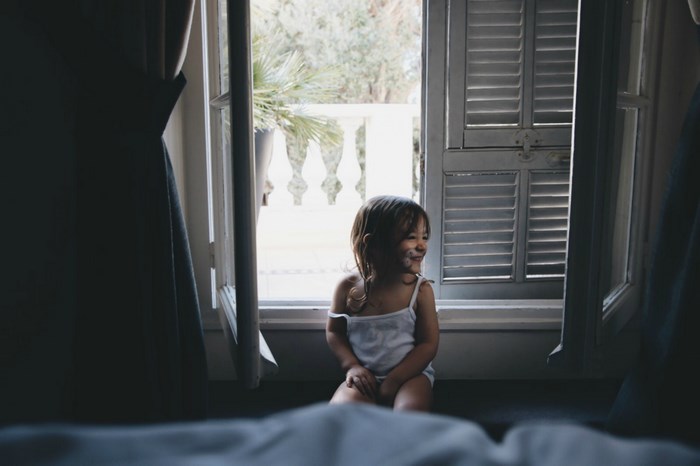 A young girl sits by an open window