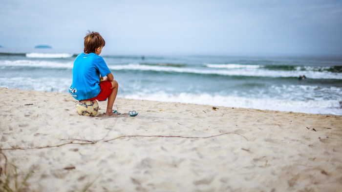Boy sitting on a soccer ball on the beach