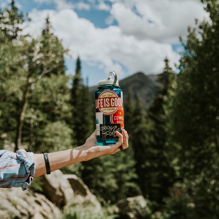Person holding a "Life is Good" water bottle in a forest