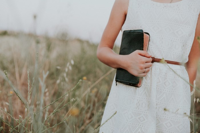 Woman in white dress holding a bible in a field