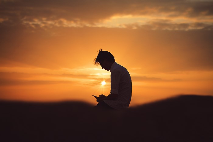 Man using phone at sunset on a hill