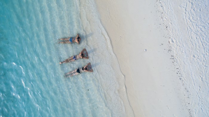 Three people relaxing in shallow turquoise water by a sandy beach